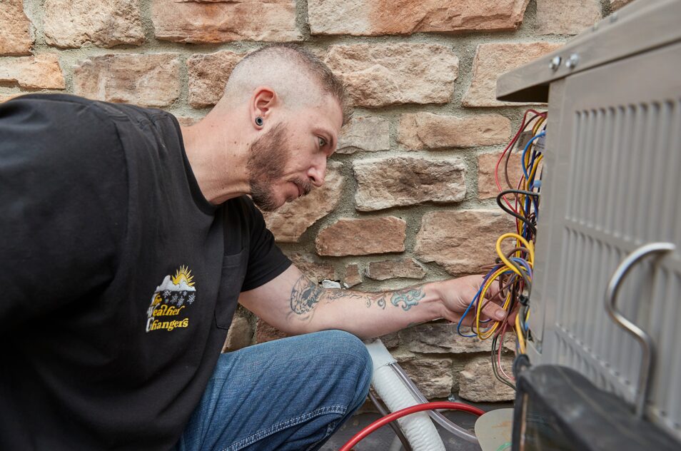 An HVAC technician with The Weather Changers inspecting electrical wiring to troubleshoot why an AC is not cooling.