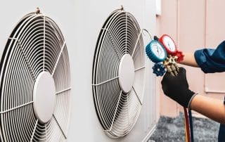 A technician testing a air conditioner with a blue and red gauge.